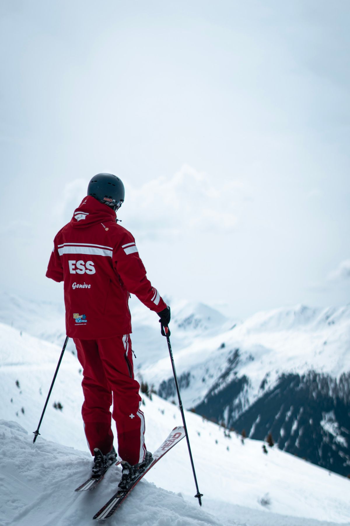 Ski instructor in red gear atop a snowy mountain overlooking a winter landscape.