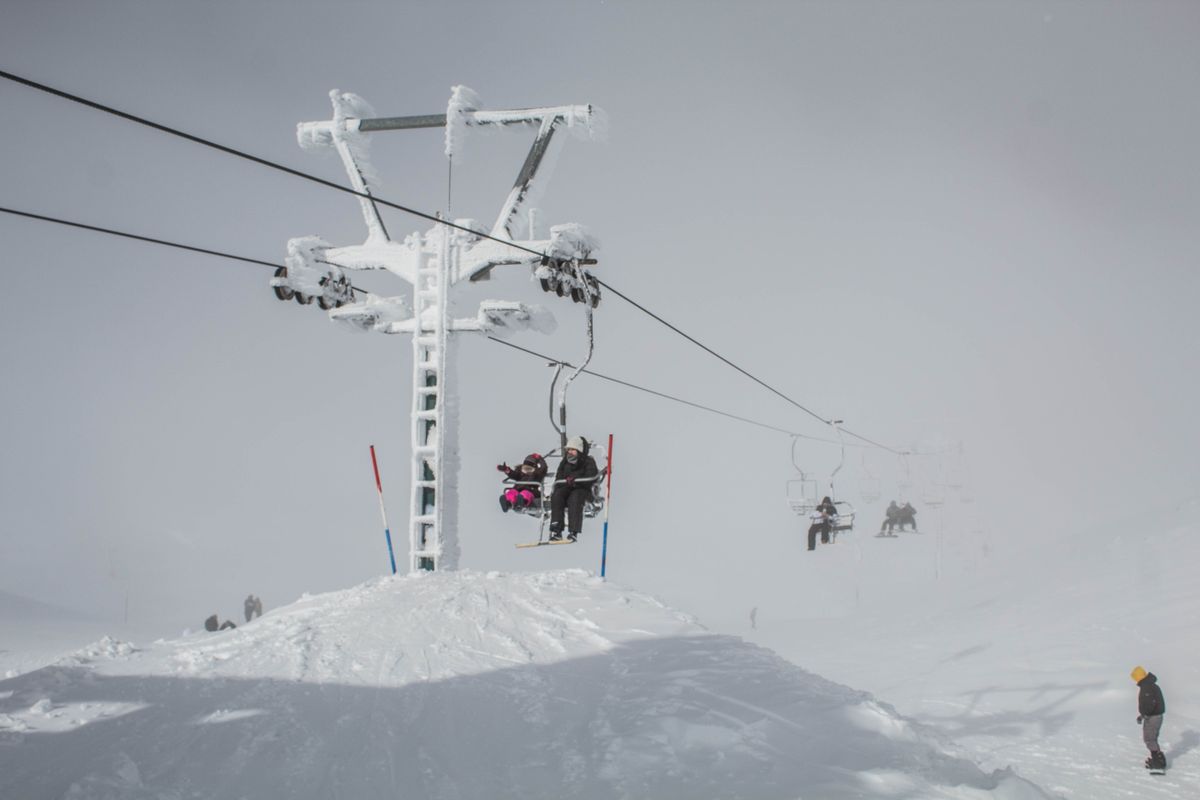 Skiers ride a snow-covered ski lift on a mountain during a winter day adding adventure to their snowy trip.