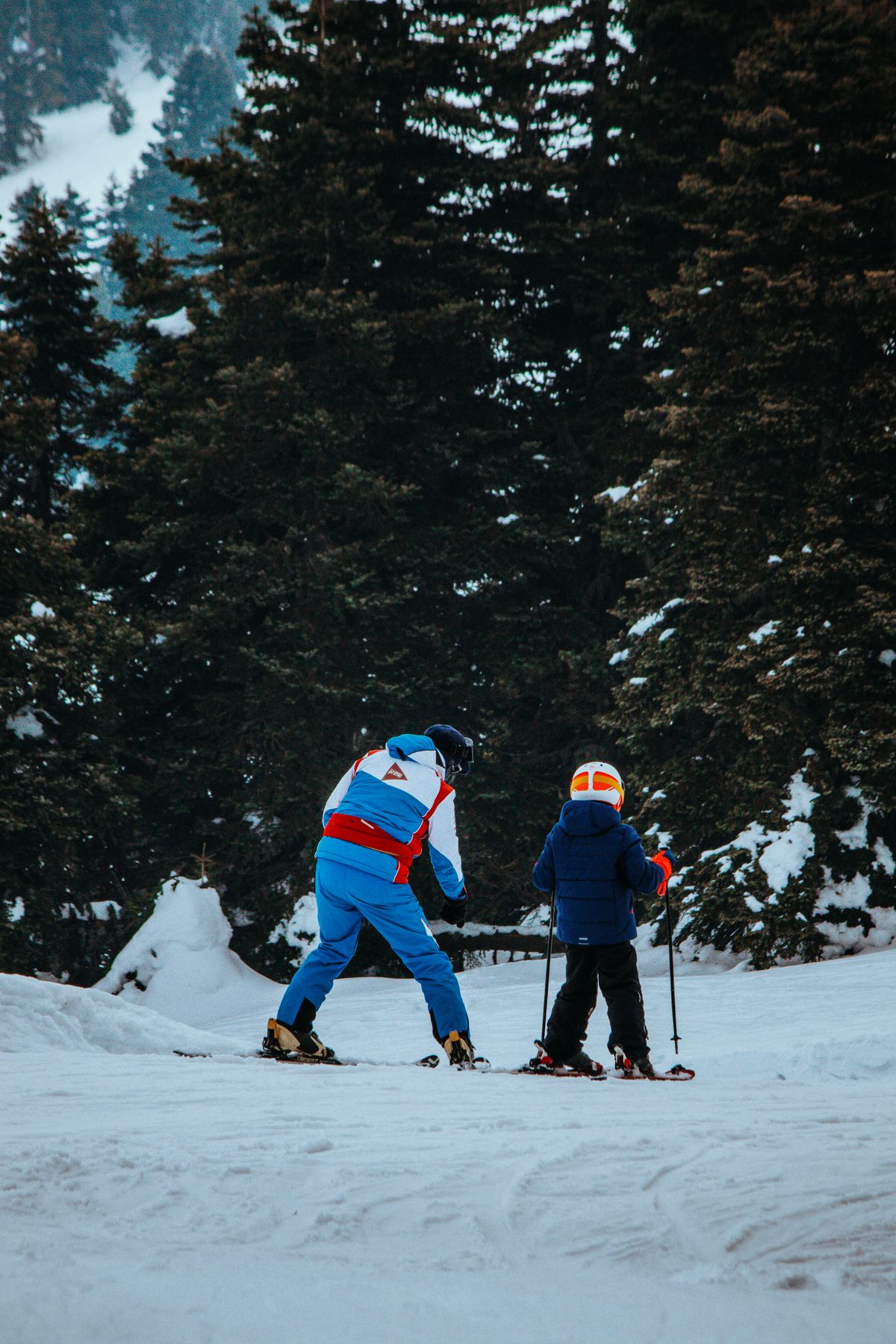 Parent and child skiing together in a snowy forest during winter.