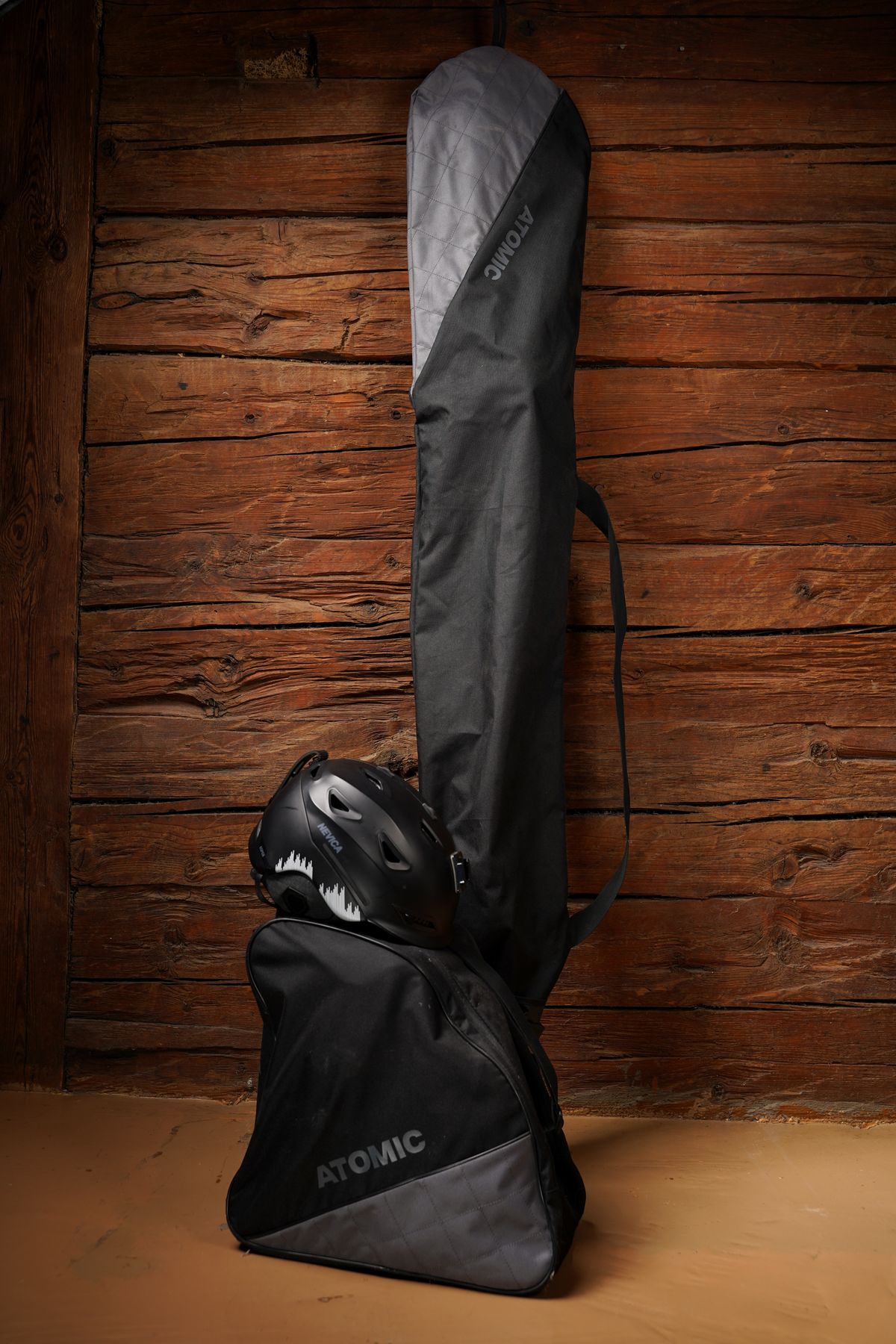 Skiing essentials including bag, helmet, ski bag against a wooden wall background.